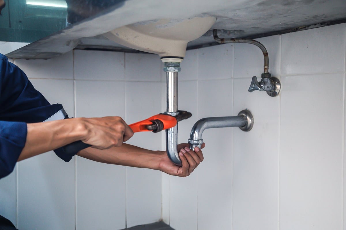 A plumber repairing a leaking sink with an adjustable wrench