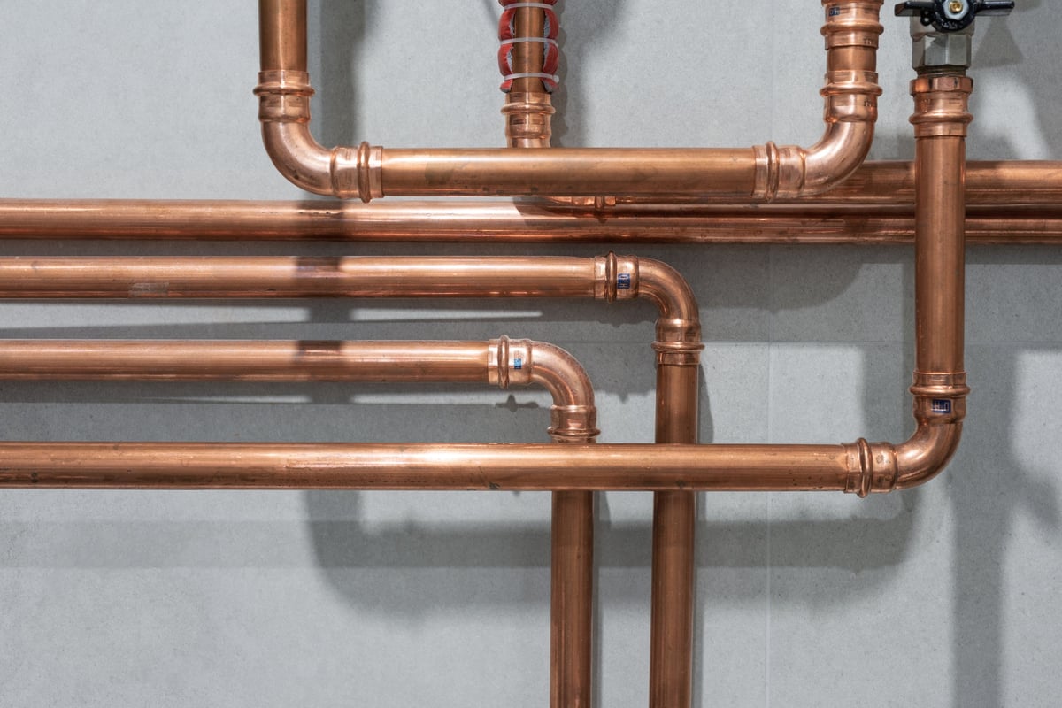 Copper pipes pressed against a grey wall tile background